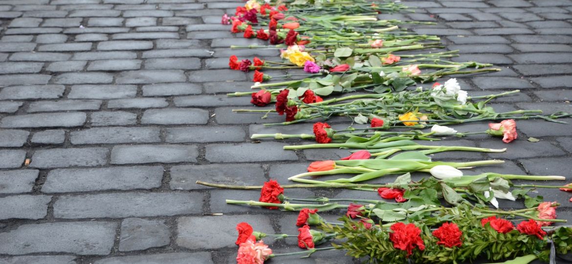 Row of red, white, and yellow flowers laid on cobblestone street in memorial tribute, symbolizing grief, remembrance, and honor.
